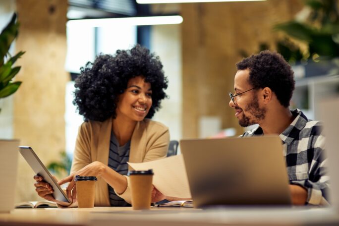 Sharing fresh ideas. Two young happy multiracial business people sitting at desk and communicating while working together in coworking space